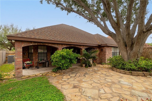 back of house featuring roof with shingles, fence, a patio area, central AC, and brick siding