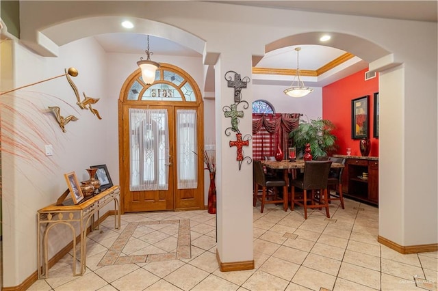 foyer entrance featuring light tile patterned floors, baseboards, a tray ceiling, and crown molding