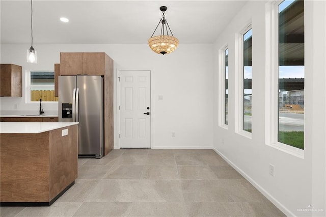 kitchen featuring brown cabinets, light countertops, decorative light fixtures, baseboards, and stainless steel refrigerator with ice dispenser