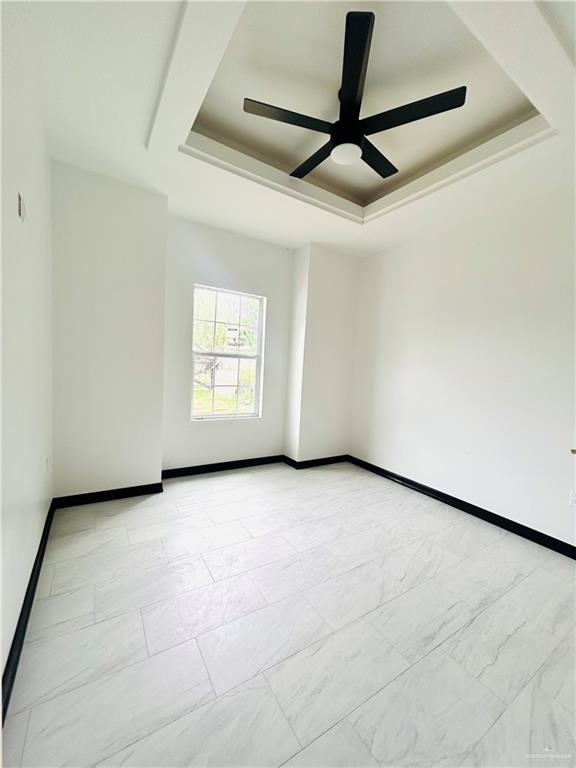 empty room with a tray ceiling, a ceiling fan, and baseboards
