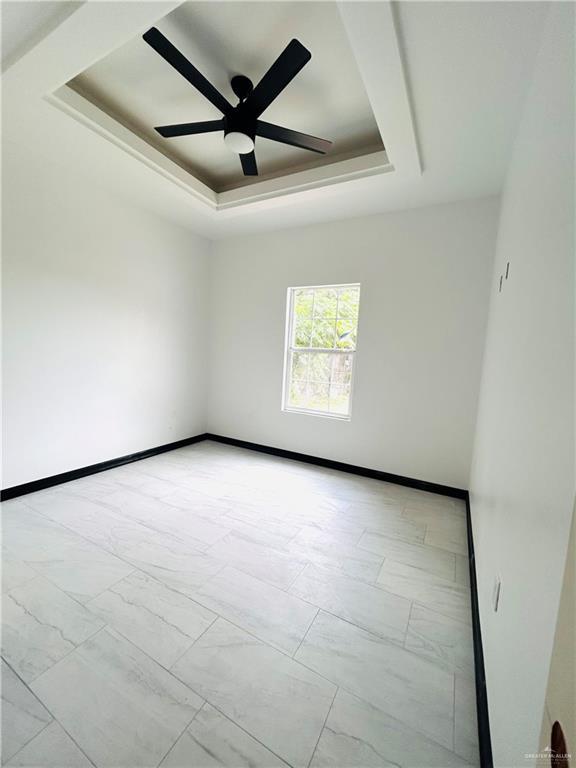 unfurnished room with a tray ceiling, marble finish floor, baseboards, and ceiling fan
