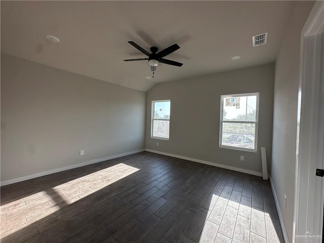 empty room with baseboards, vaulted ceiling, dark wood-style floors, visible vents, and ceiling fan