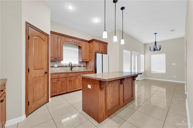 3120 La Puerta Ave, Edinburg, TX 78541 - kitchen with freestanding refrigerator, a breakfast bar, a kitchen island, brown cabinetry, and light stone countertops