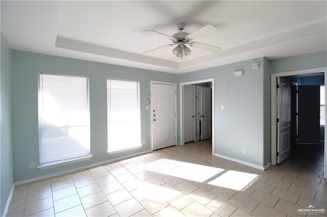 tiled empty room with a raised ceiling and ceiling fan