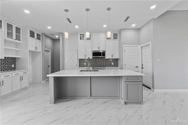 519 Oriole Dr, Los Fresnos, TX 78566 - kitchen featuring stainless steel microwave, decorative backsplash, white cabinets, marble finish floor, and a kitchen island with sink