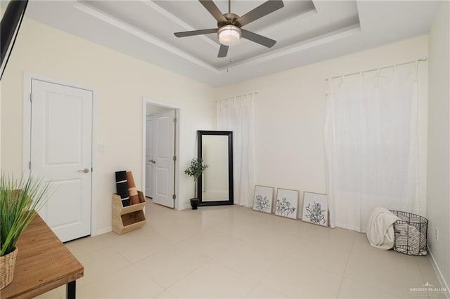 tiled empty room featuring ceiling fan and a tray ceiling