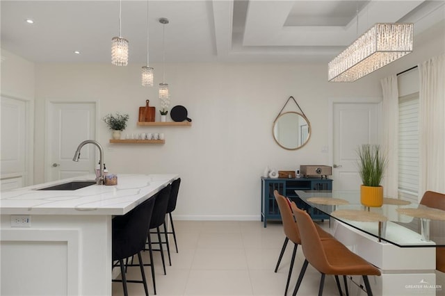 kitchen featuring light stone countertops, sink, hanging light fixtures, a notable chandelier, and a center island with sink