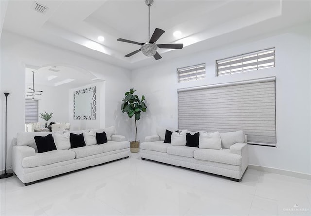 tiled living room with a tray ceiling and ceiling fan