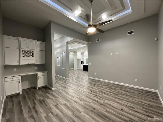 unfurnished office with built in desk, wood finished floors, a ceiling fan, visible vents, and baseboards