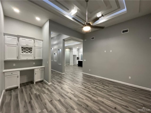 unfurnished office with built in desk, a ceiling fan, dark wood finished floors, visible vents, and baseboards