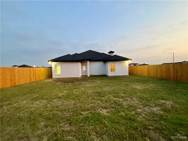 back of property at dusk featuring a lawn and a fenced backyard