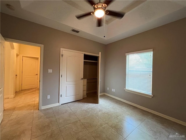 unfurnished bedroom featuring light tile patterned flooring, ceiling fan, a tray ceiling, and a closet