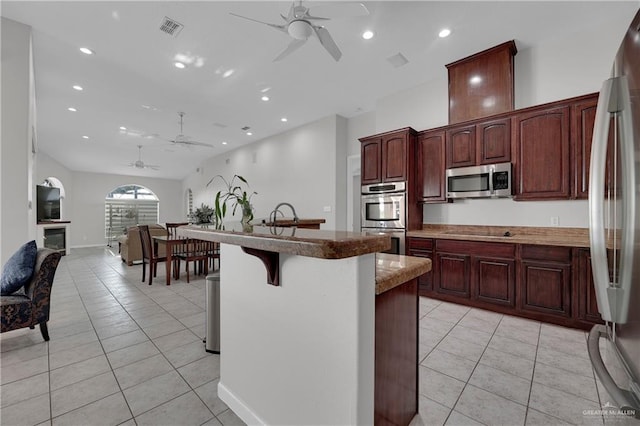 kitchen featuring appliances with stainless steel finishes, a breakfast bar, ceiling fan, a kitchen island with sink, and light tile patterned flooring