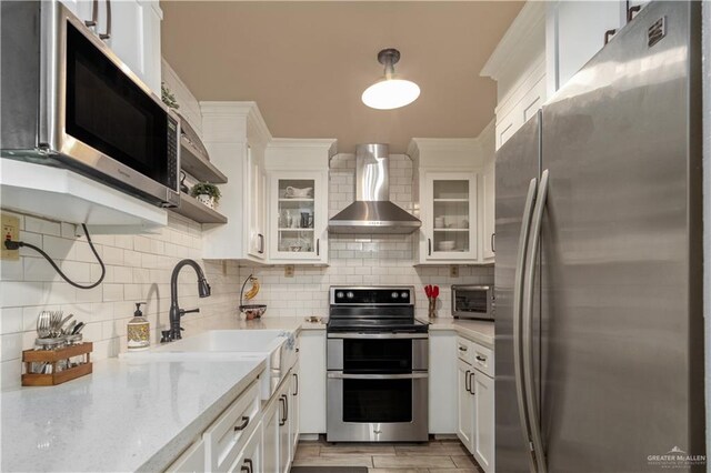 1309 El Camino Dr, Weslaco, TX 78599 - kitchen with stainless steel appliances, wall chimney range hood, decorative backsplash, and white cabinets