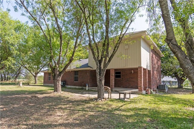 1309 El Camino Dr, Weslaco, TX 78599 - rear view of house with brick siding, a patio area, central air condition unit, and a lawn