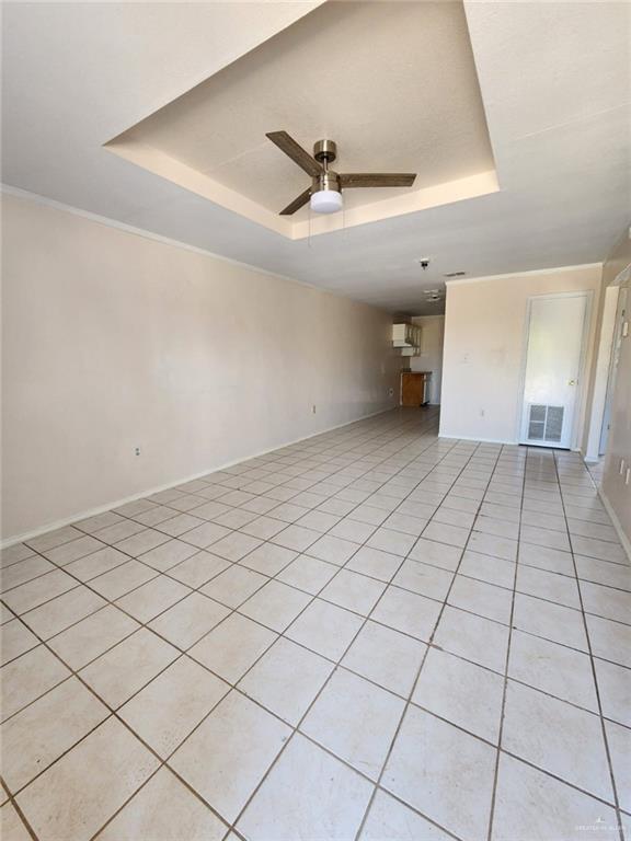 unfurnished living room with ceiling fan, light tile patterned floors, and a tray ceiling