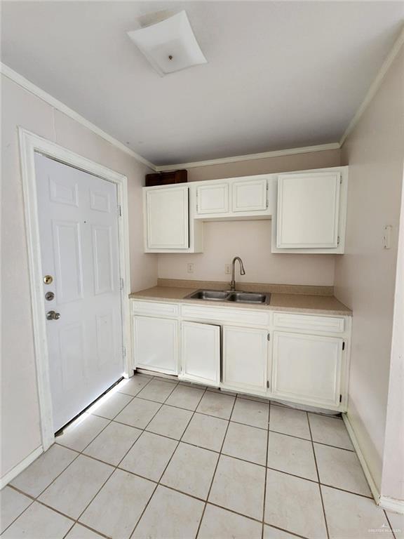 kitchen featuring white cabinetry, sink, light tile patterned flooring, and ornamental molding