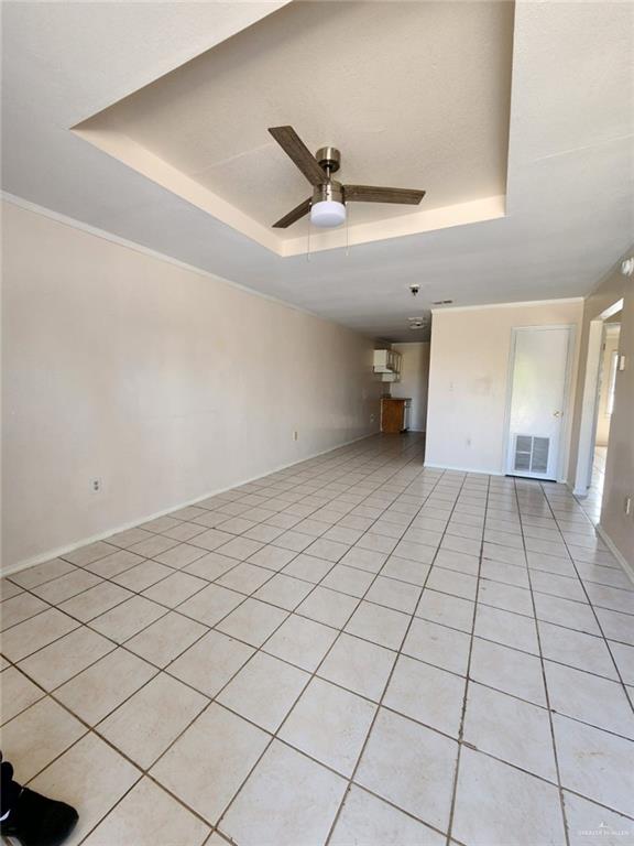 unfurnished living room with a raised ceiling, ceiling fan, and light tile patterned flooring