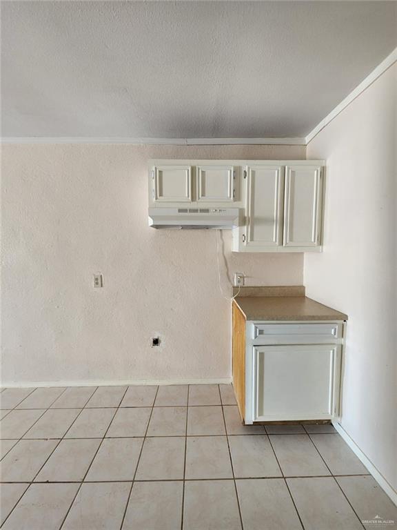 interior space with ornamental molding, a textured ceiling, and light tile patterned floors