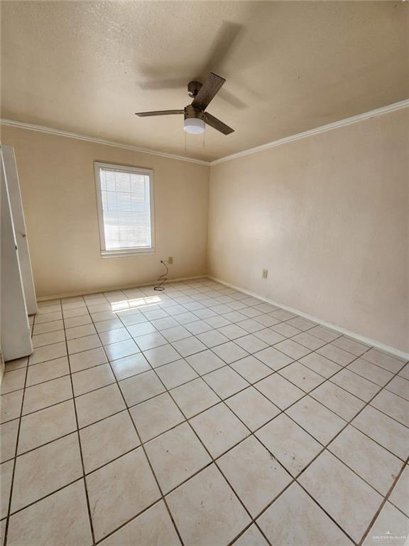 spare room featuring ceiling fan, crown molding, and light tile patterned floors