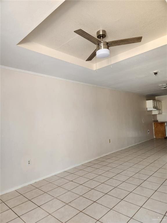 tiled spare room featuring ceiling fan, a raised ceiling, and crown molding