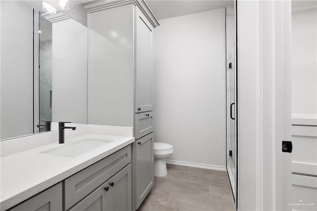 bathroom with vanity, a shower stall, toilet, and baseboards