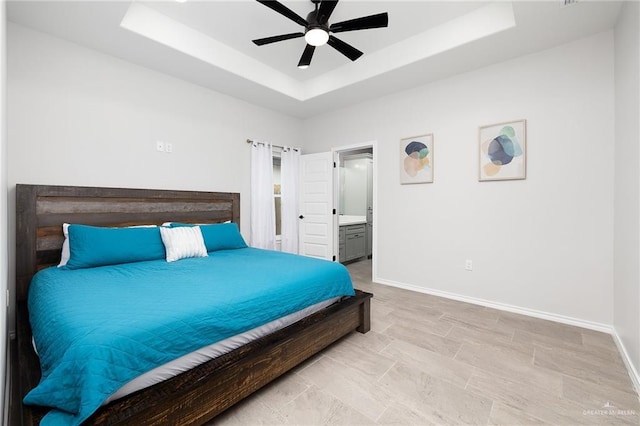 bedroom with baseboards, a raised ceiling, a ceiling fan, and ensuite bathroom
