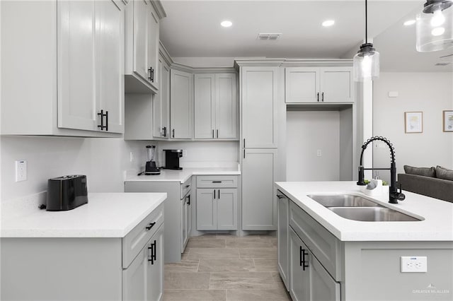 kitchen featuring a center island with sink, visible vents, gray cabinetry, a sink, and decorative light fixtures