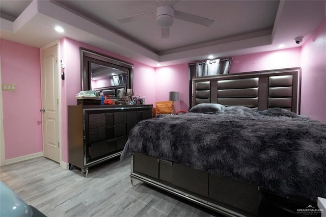 bedroom with ceiling fan, light hardwood / wood-style floors, and a raised ceiling