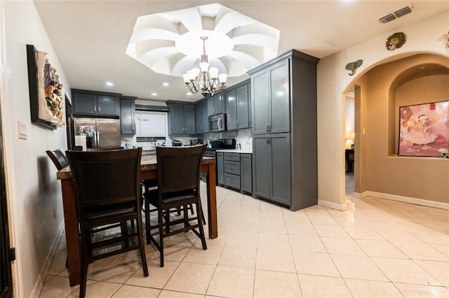 kitchen with decorative backsplash, stainless steel appliances, light tile patterned floors, a notable chandelier, and hanging light fixtures