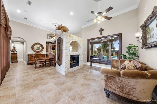 living room featuring crown molding, a stone fireplace, ceiling fan, and a high ceiling