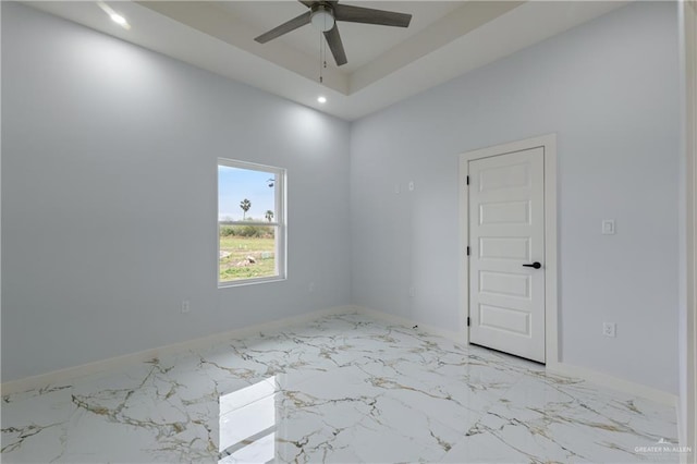 empty room featuring baseboards, a tray ceiling, recessed lighting, marble finish floor, and a ceiling fan