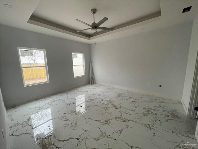 empty room with a tray ceiling, marble finish floor, and ceiling fan