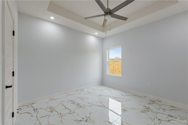 empty room with recessed lighting, marble finish floor, a raised ceiling, and baseboards