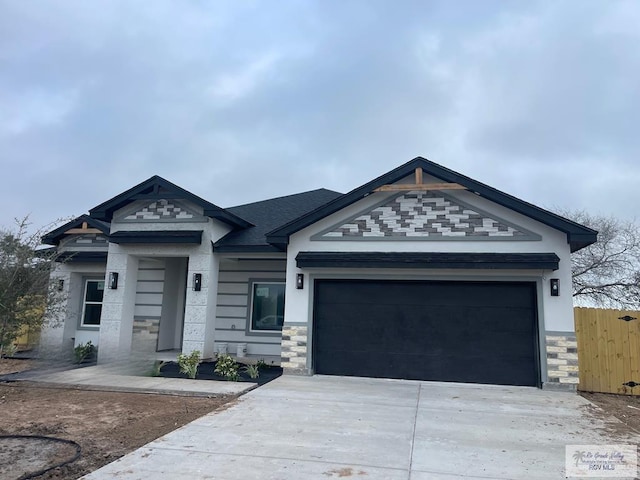 view of front of home featuring stone siding, driveway, an attached garage, and fence