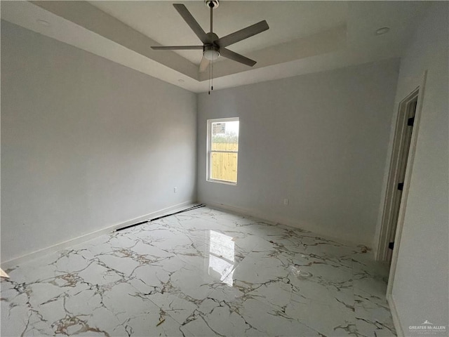 spare room featuring a tray ceiling, baseboards, marble finish floor, and ceiling fan