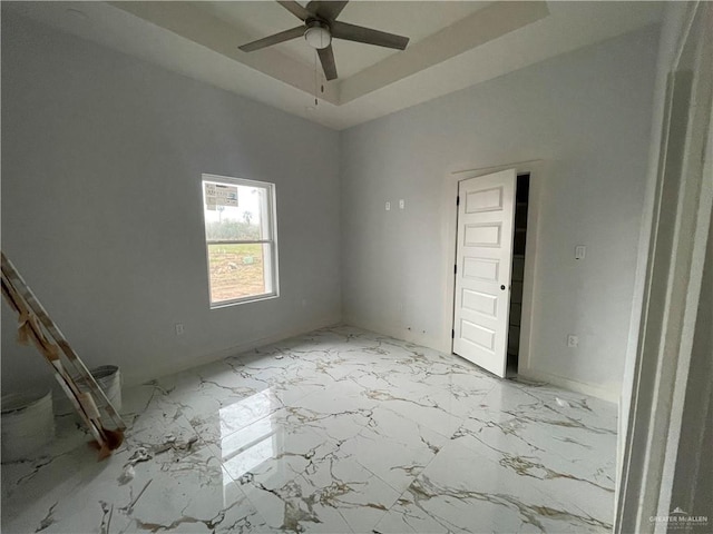 spare room featuring marble finish floor, a raised ceiling, and a ceiling fan