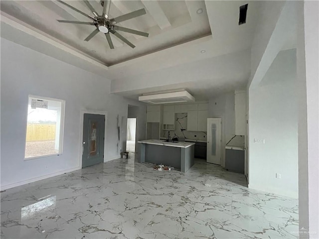 unfurnished living room featuring ceiling fan, a raised ceiling, sink, and a towering ceiling