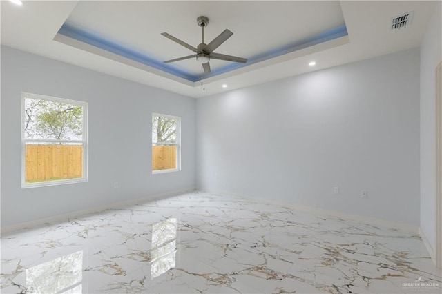 empty room with visible vents, a raised ceiling, marble finish floor, and ceiling fan