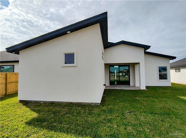 back of house featuring a lawn, fence, and stucco siding