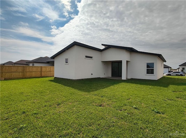 rear view of property with a yard, fence, and stucco siding