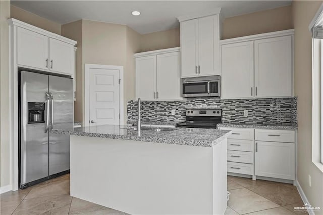 kitchen with white cabinetry, decorative backsplash, a sink, appliances with stainless steel finishes, and a kitchen island with sink