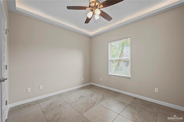 empty room with a ceiling fan, a tray ceiling, marble finish floor, and baseboards