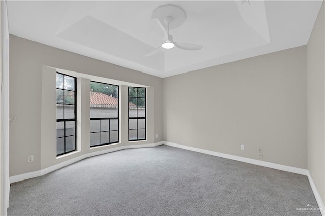carpeted empty room featuring baseboards, a tray ceiling, and ceiling fan