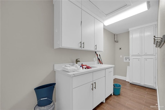 laundry room featuring cabinet space, wood finish floors, a sink, baseboards, and hookup for an electric dryer