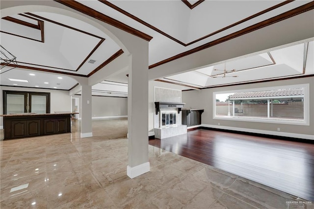 unfurnished living room with visible vents, arched walkways, baseboards, a glass covered fireplace, and ornamental molding