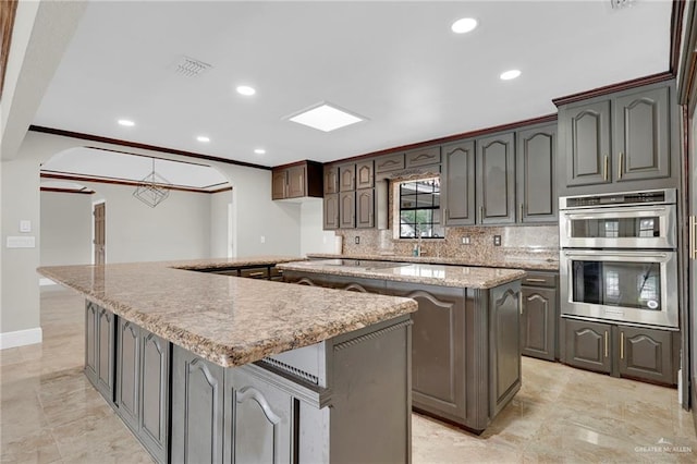 kitchen with double oven, arched walkways, a center island, decorative backsplash, and visible vents