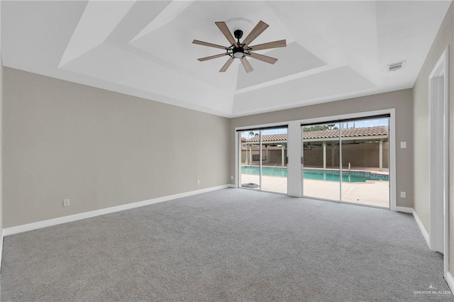 empty room with visible vents, carpet floors, baseboards, ceiling fan, and a raised ceiling