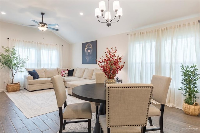 dining space with hardwood / wood-style flooring, ceiling fan with notable chandelier, and vaulted ceiling