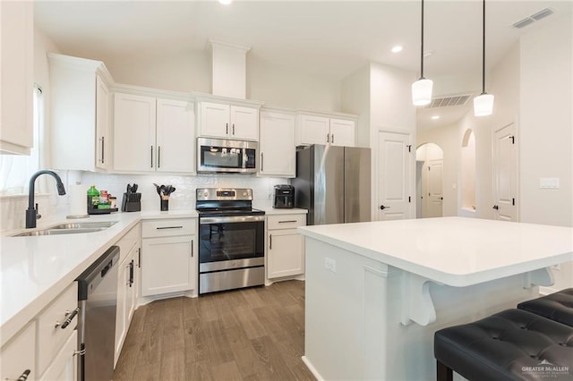 kitchen featuring sink, white cabinetry, hanging light fixtures, stainless steel appliances, and backsplash